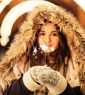 Woman in winter coat and mittens holding sparkler